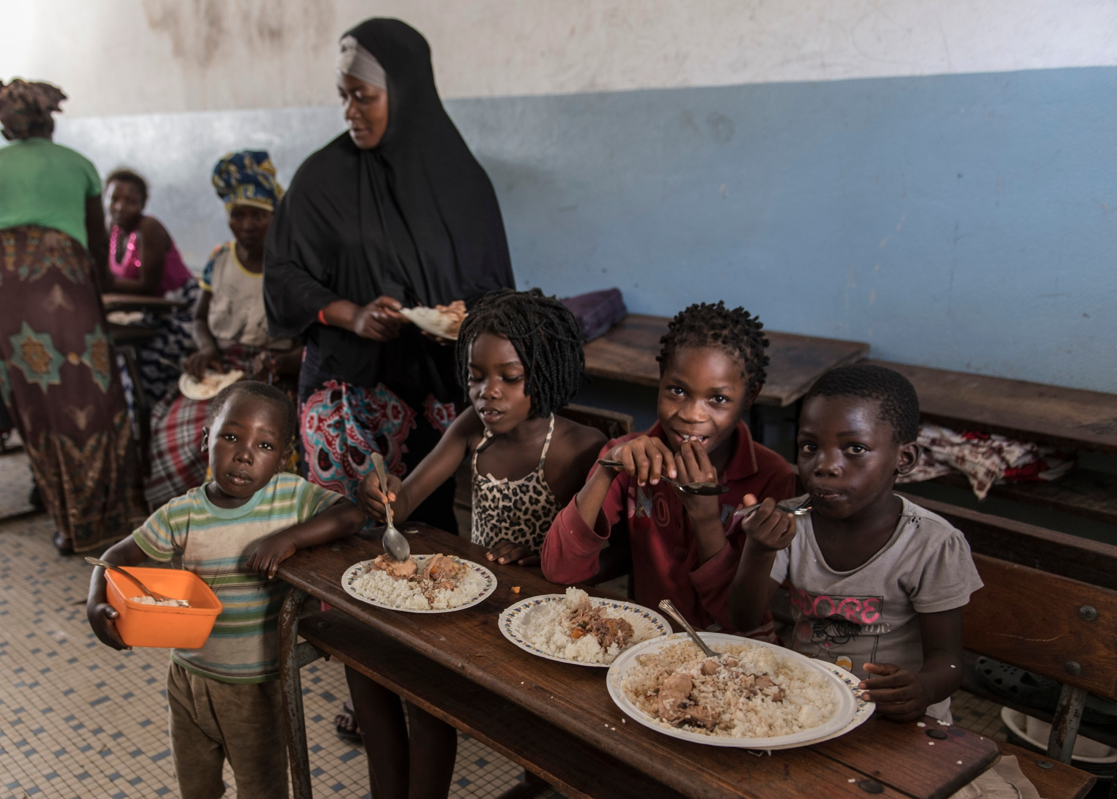 Young children sat at a table with plates of food, looking at the camera.